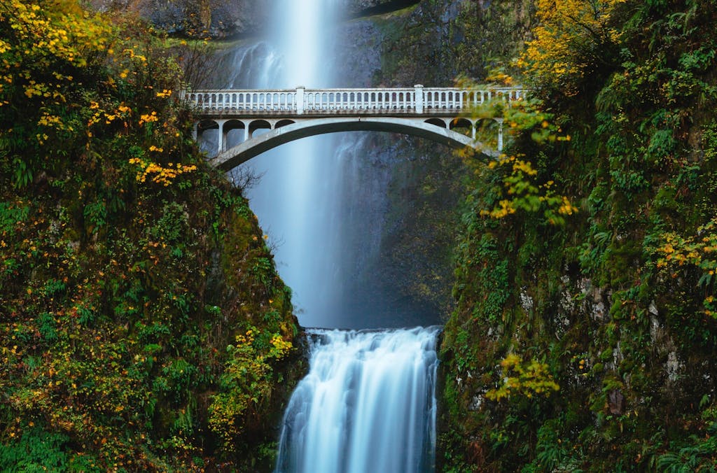 a large waterfall in a forest with a bridge in the background