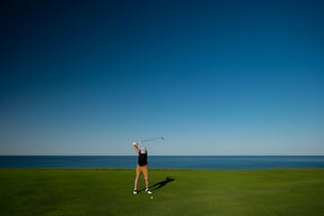 man golfing with water behind him and blue skies
