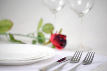 Cutlery and plates on a white background glasses of wine and red rose