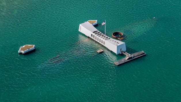 a small boat in a body of water with USS Arizona Memorial in the background