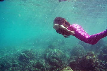 A mermaid swimming away from the camera and towards the surface of the water in Honolulu, HI