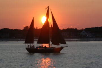 A silhouette of the Pineapple Ketch's masts against Maine's sunset sky