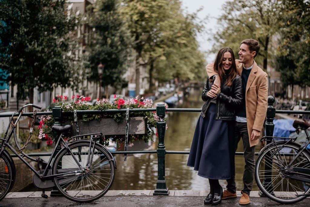 Couple laughing holding hands on a bridge in Amsterdam next to bikes and flowers