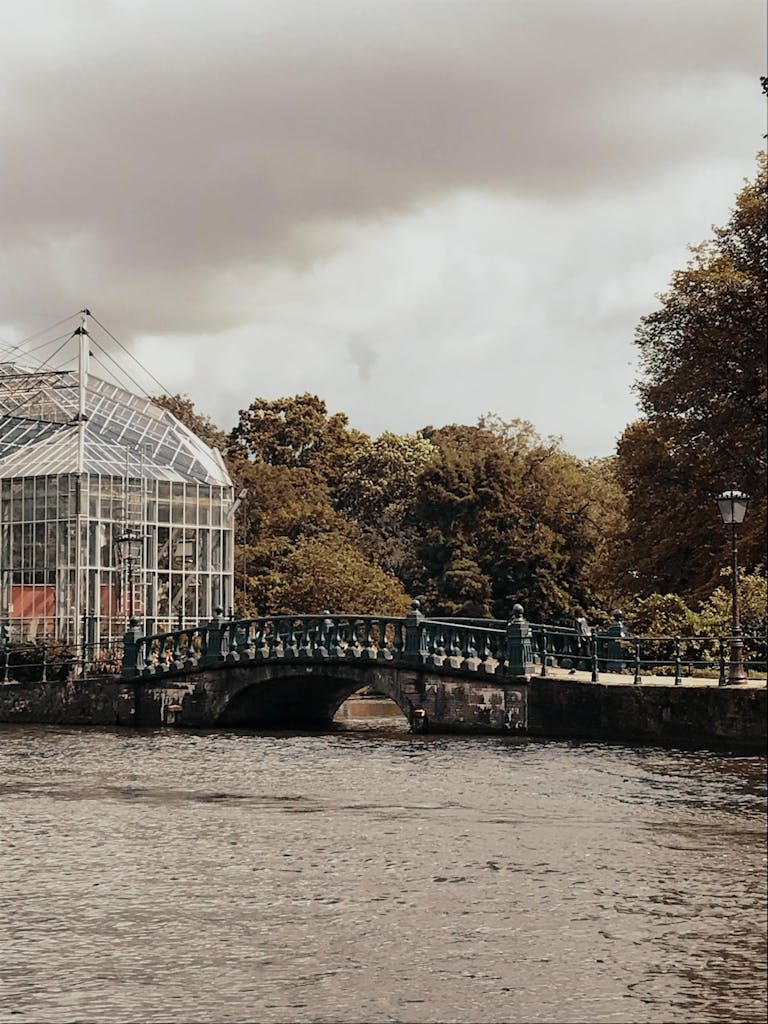 a bridge over the water and trees next to botanical garden in Amsterdam