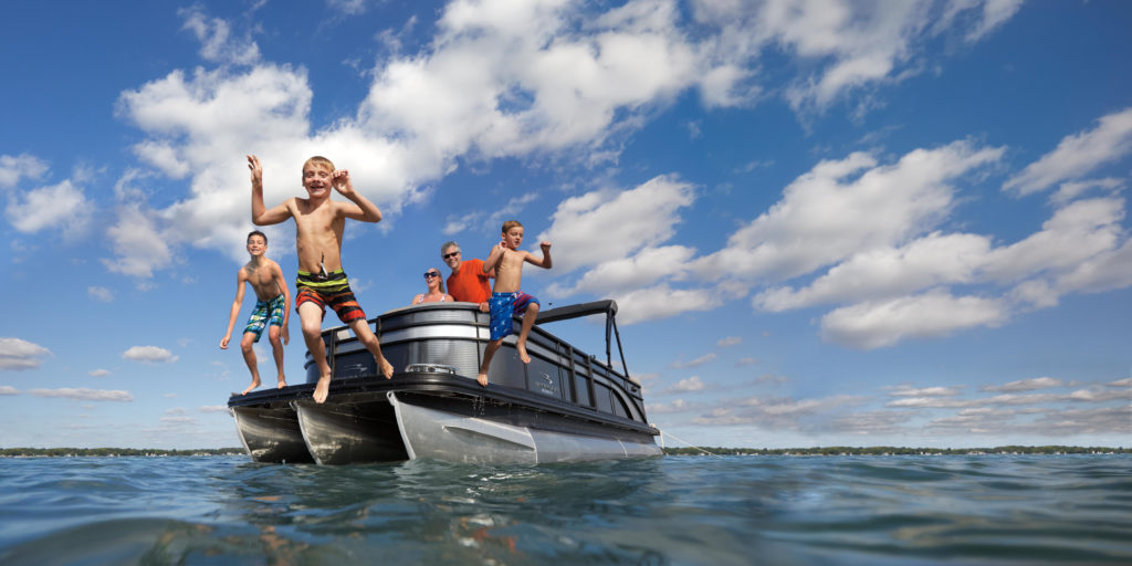 kids jumping off the back of a pontoon boat into the water