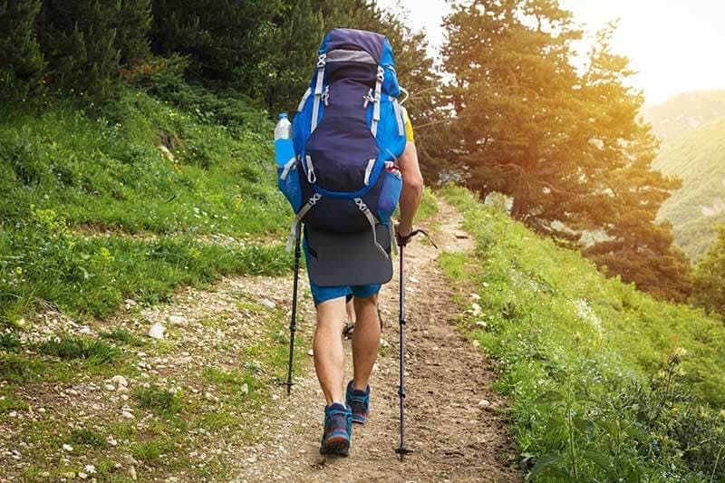 A man wearing a backpack while hiking on a dirt trail