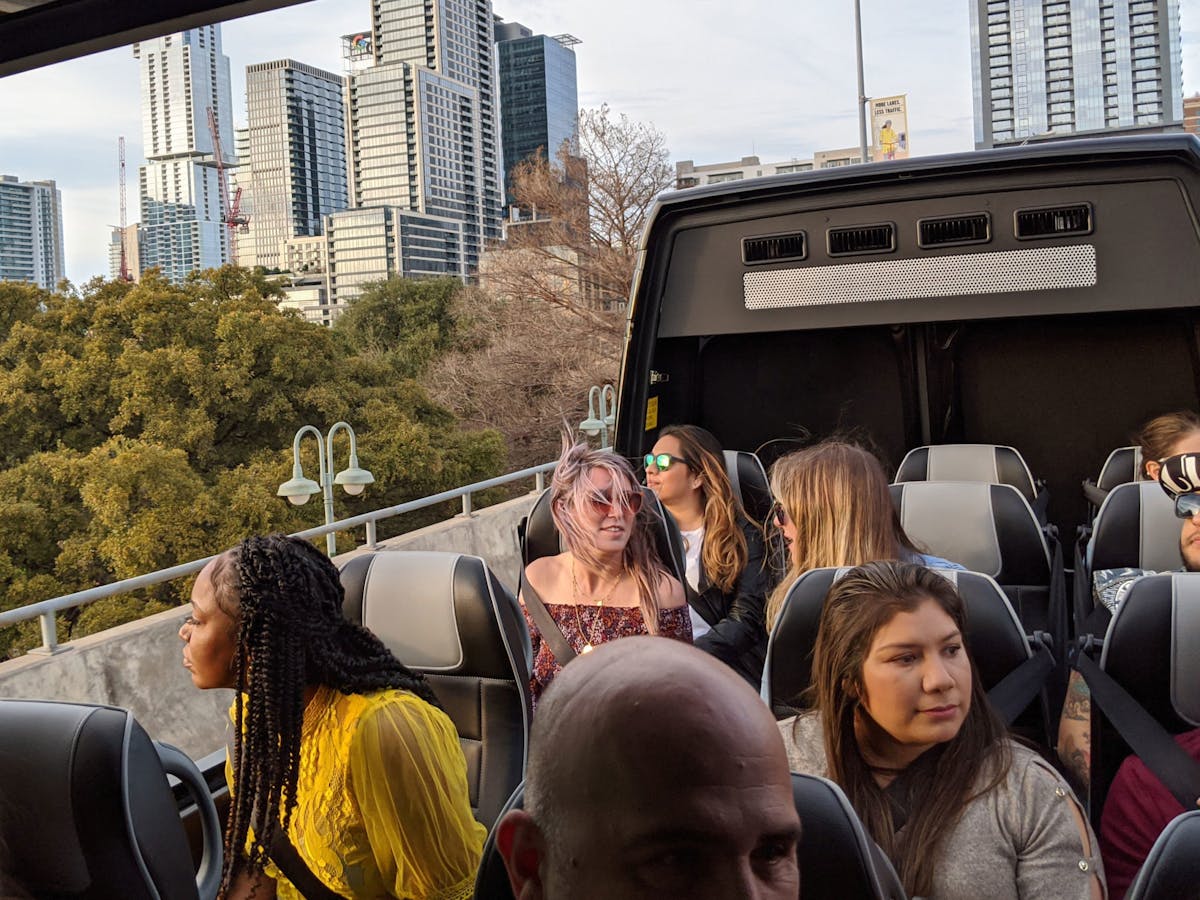 People sitting in panoramic bus with the top open. Austin skyline in the background.