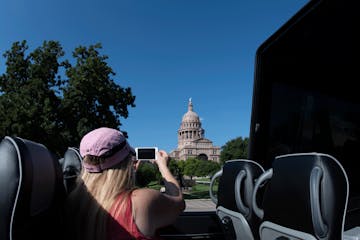 Blond woman with pink hat taking a photo of the Texas Capitol