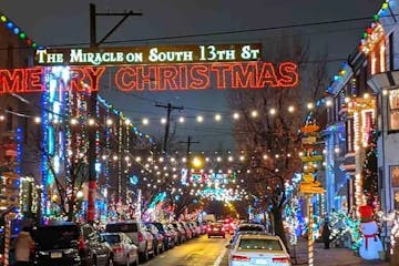 The 1600 block of South 13th Street is all lit up with Christmas lights and decorations for the annual Miracle on South 13th Street Christmas lights event. Two signs made of Christmas lights hang from phone lines in the foreground with 