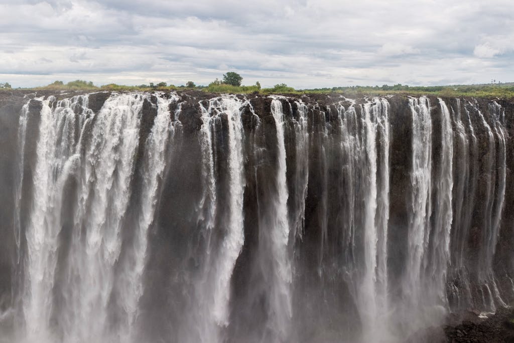 a large waterfall Victoria Falls Tours 2022over some water with Victoria Falls in the background