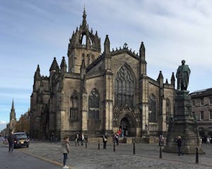 a group of people walking in front of a church with St Giles' Cathedral in the background