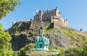 a large stone statue in front of a castle with Edinburgh Castle in the background