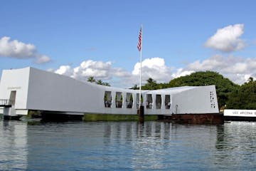 a small boat in a large body of water with USS Arizona Memorial in the background