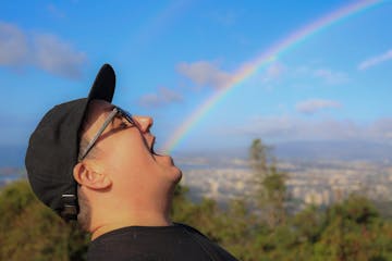 a man wearing a hat and a rainbow in the sky