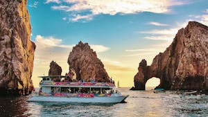 a small boat in a body of water with Arch of Cabo San Lucas in the background