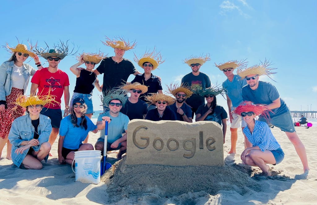 a group of people posing for a picture behind a sand castle that says google