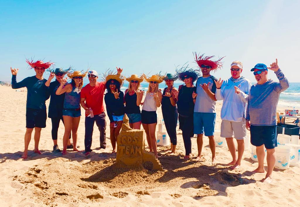 a group of people standing on top of a sandy beach behind a sand castle