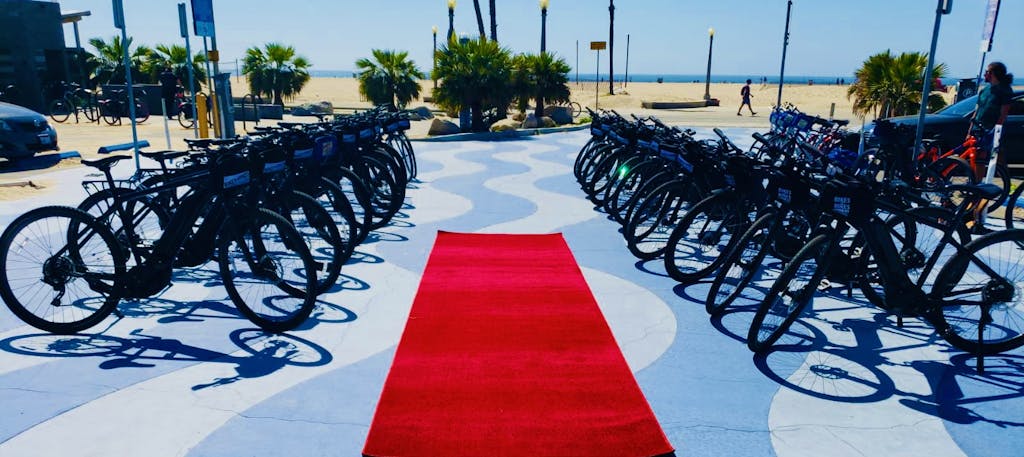 a row of bicycles lined up next to a red carpet in venice california