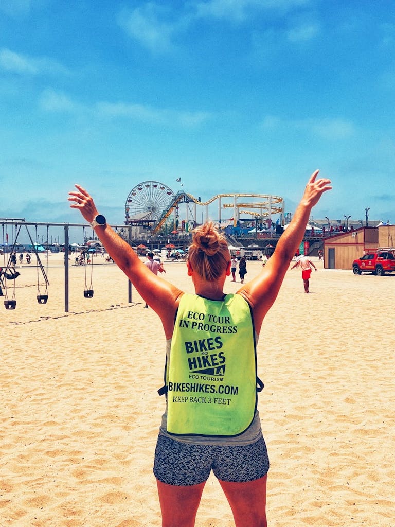 a person throwing their hands in the air by the santa monica pier on a los angeles bike tour