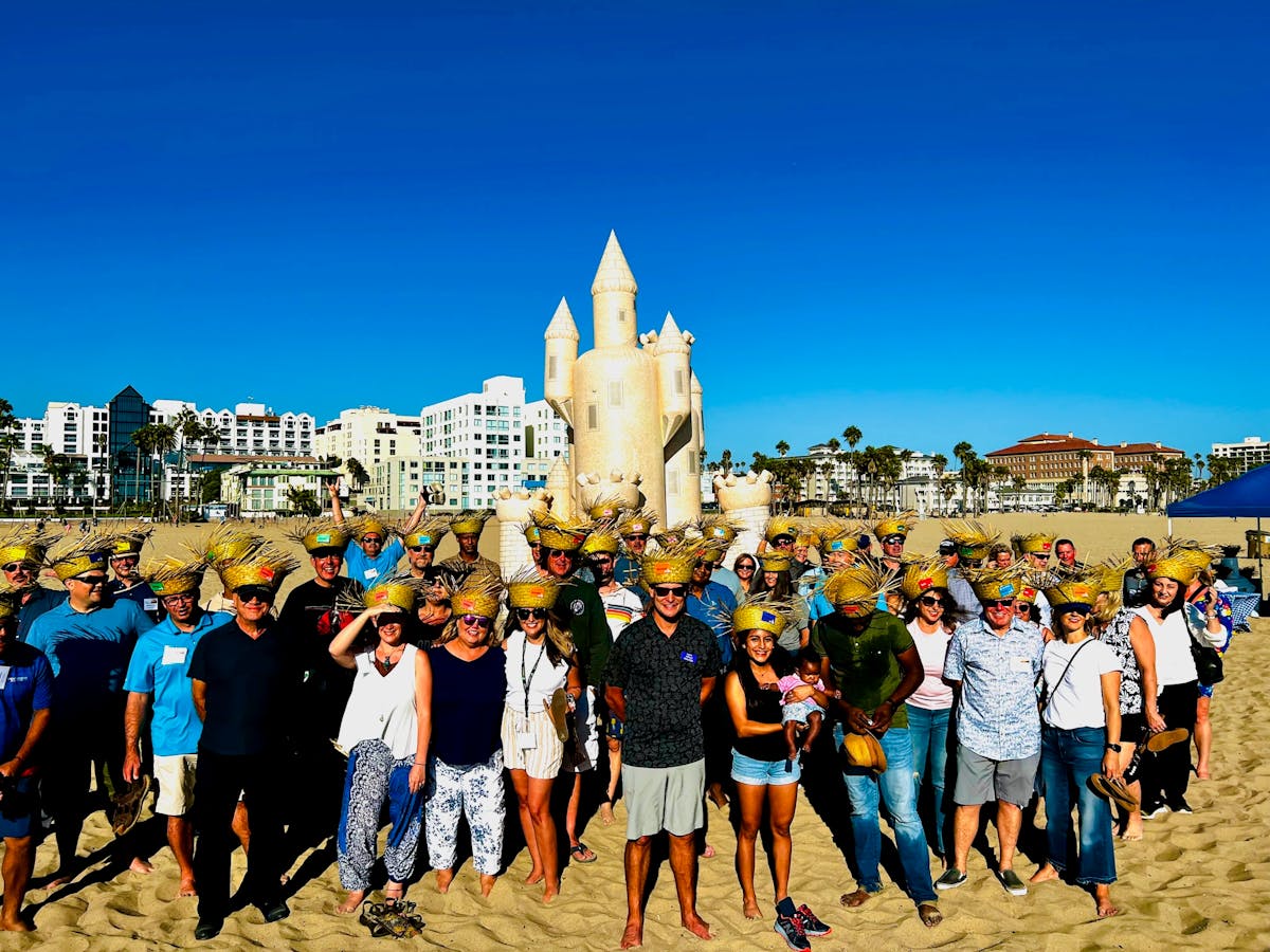 a group of people standing in front of a crowd posing for the camera in front of a sand castle doing group team building in los angeles