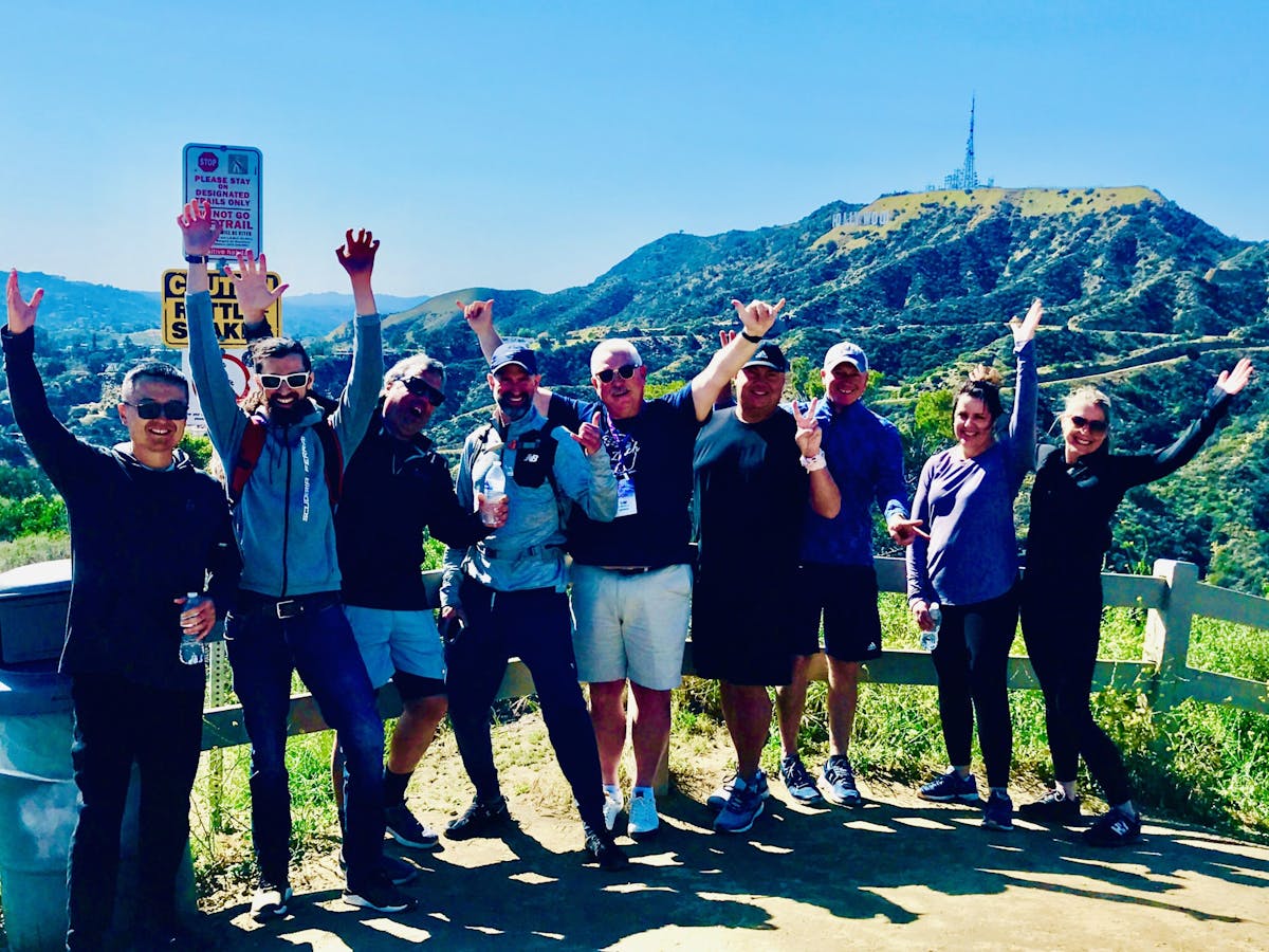 a group of people standing in front of the hollywood sign on a team building tour