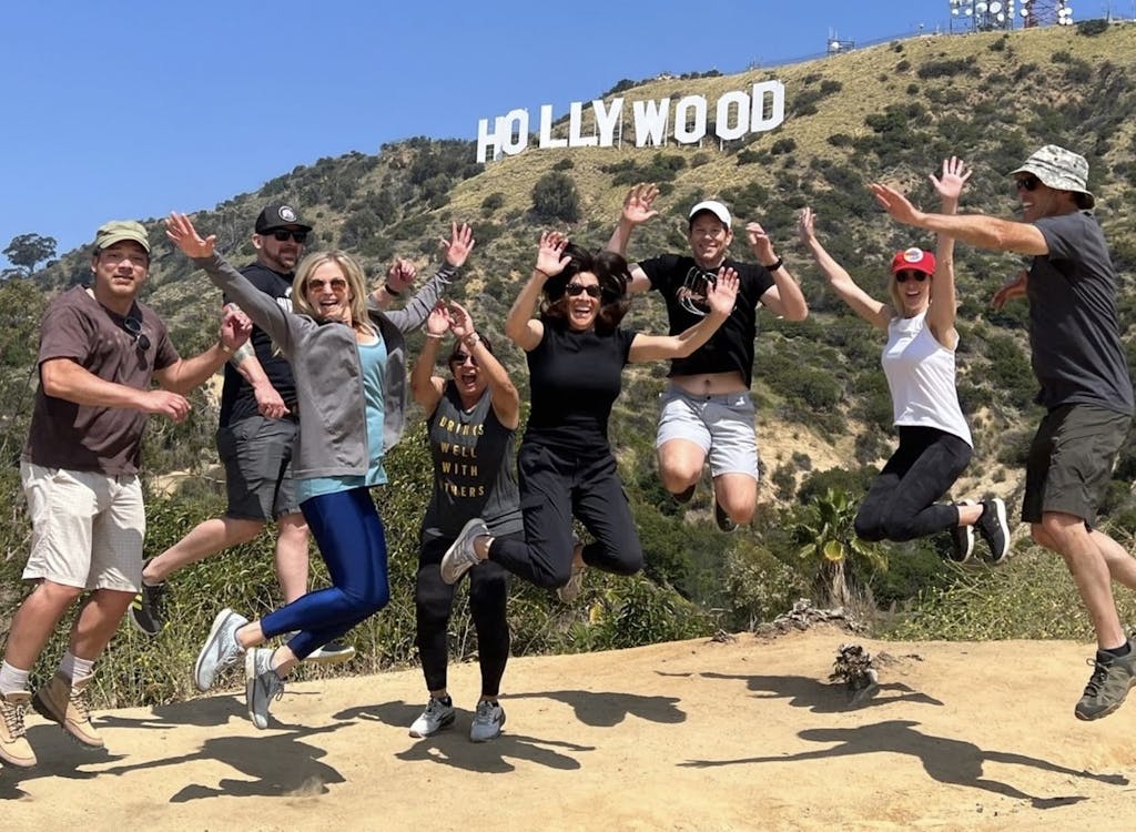 a group of people jumping in the air beneath the hollywood sign on a hollywood tour
