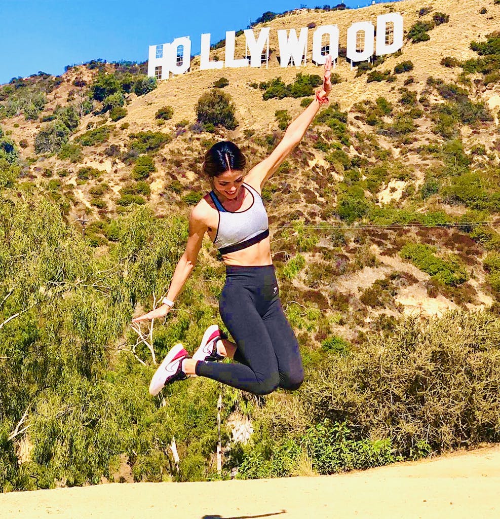 a girl jumps in the air below the hollywood sign