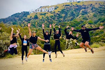 a group of people jumping in the air in front of the hollywood sign