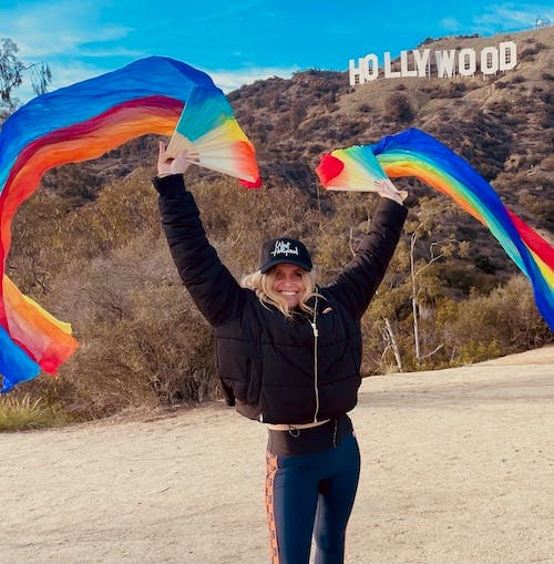 a person waving two rainbow flags under the hollywood sign