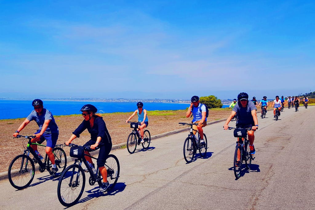 a group of people riding bicycles on a beach bike tour of la