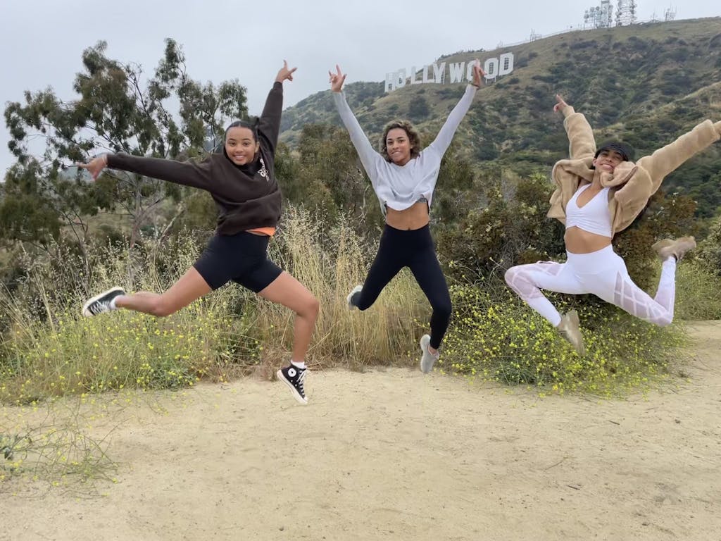 three people jumping into the air below the hollywood sign on a los angeles tour