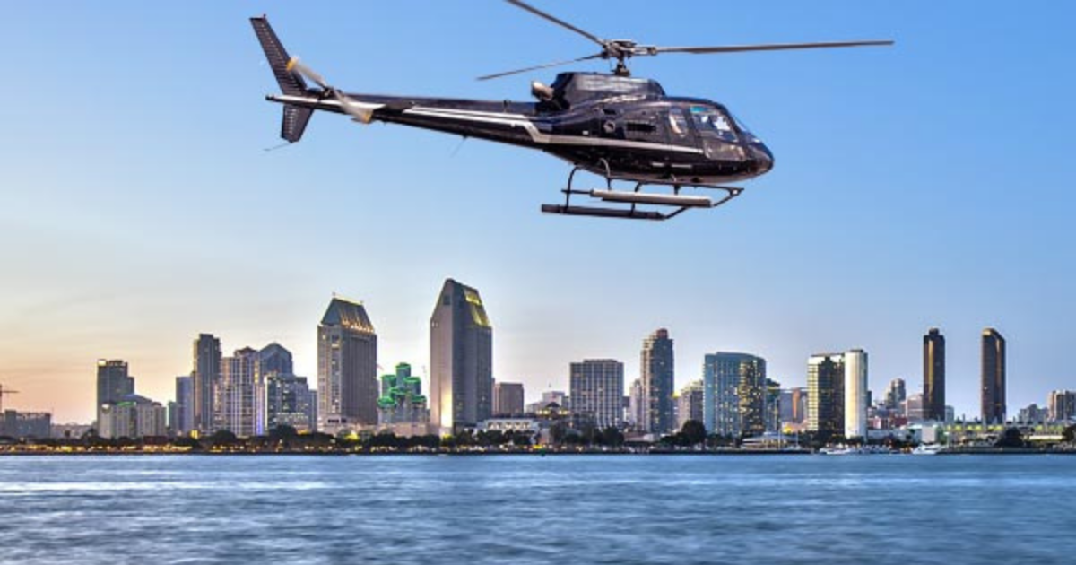 a helicopter flying over a body of water with a city in the background
