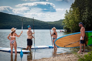 a couple of people that are standing in the water with paddles, as one person carries a paddleboard into the lake