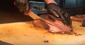 gloved hands cutting a large piece of beef with a large knife