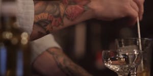 tattooed arms mixing a cocktail in a glass