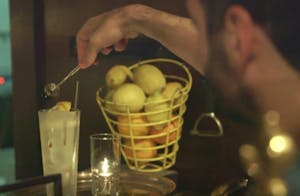 a person mixing a cocktail next to a bucket of lemons