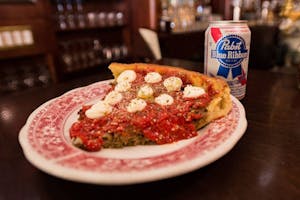 a close up of a slice of pizza and a Blue Ribbon beer on a table