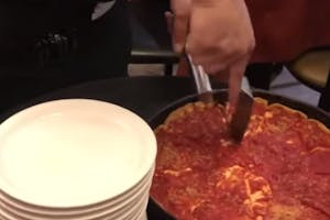 a pizza in a on being cut next to a stack of white plates