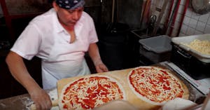 a man preparing two pizzas on a wooden cutting board