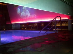 an indoor pool with lights, a bar and a large overhead digital screen