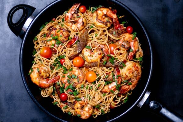 a skillet with pasta, shrimp and tomatoes