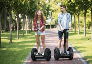 a man and woman riding down a path lined with trees, riding segways