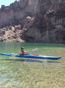 a woman in a long blue kayak on crystal clear water kayaking down the Colorado River