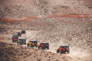 a line of Jeeps going up a barren dessert sandy road