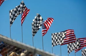 alternating american flags and checkered flags floating in the wind with the clear blue sky in the background