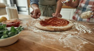 two people working together to make a homemade pizza