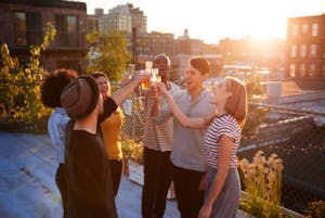 a group of people standing on a rooftop with drinks at sunset