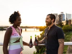 a man and a woman with drinks chatting outside near a bridge at sunset