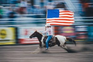 a man riding a horse while holding a flag at a rodeo