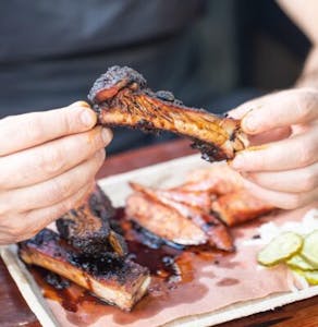 hands holding a rib over a plate of ribs